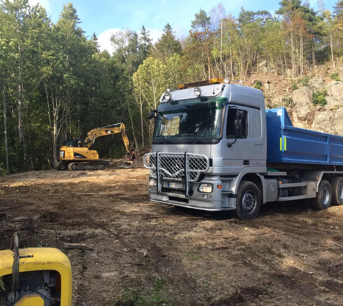 Lastebil foran gravemaskin i arbeid med tomt i skog